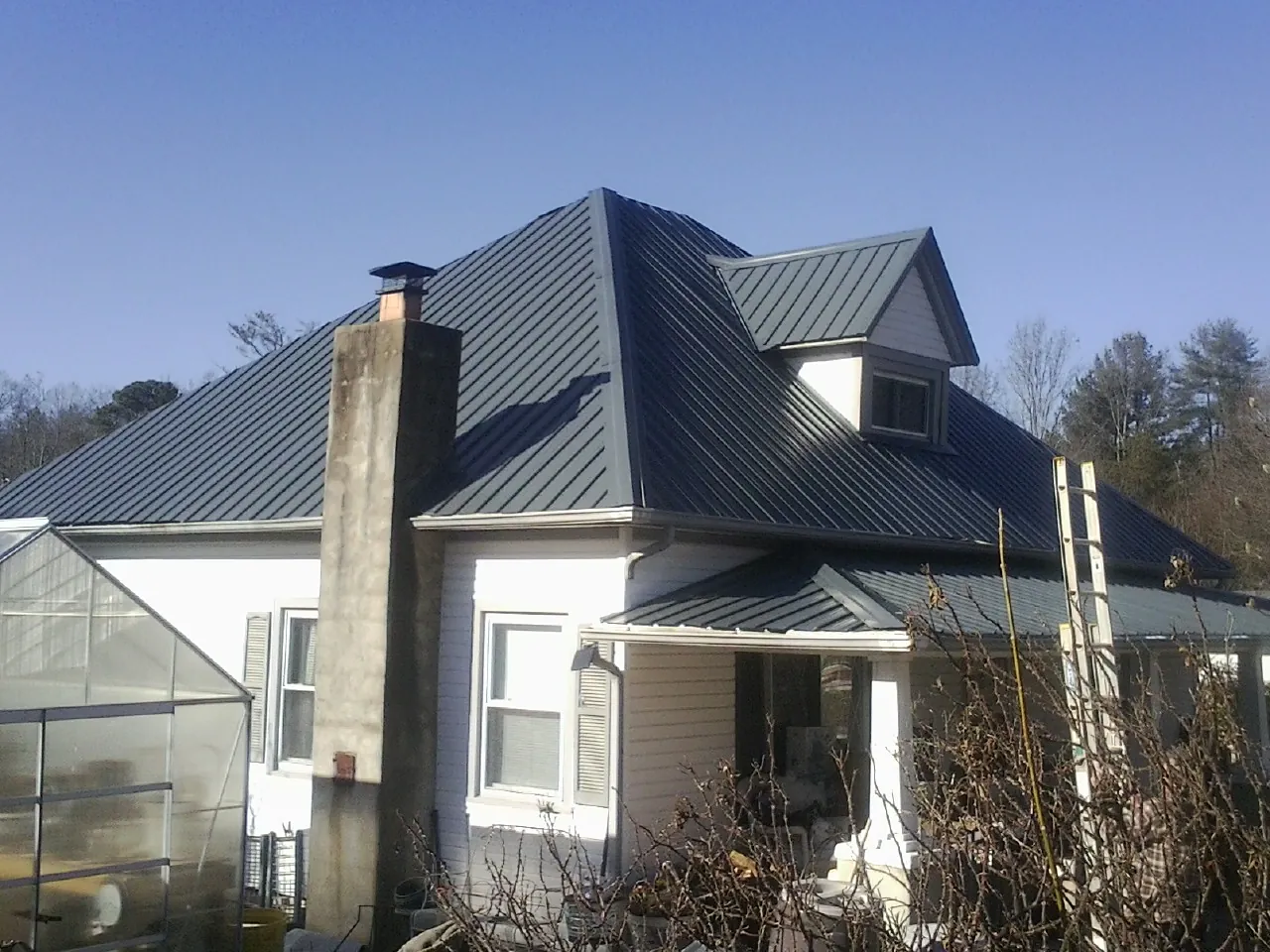 Dark blue standing seam metal roof on a white farmhouse with dormer — Slate & Tile Roof Repair by Roofing Brothers in Cedarpines Park