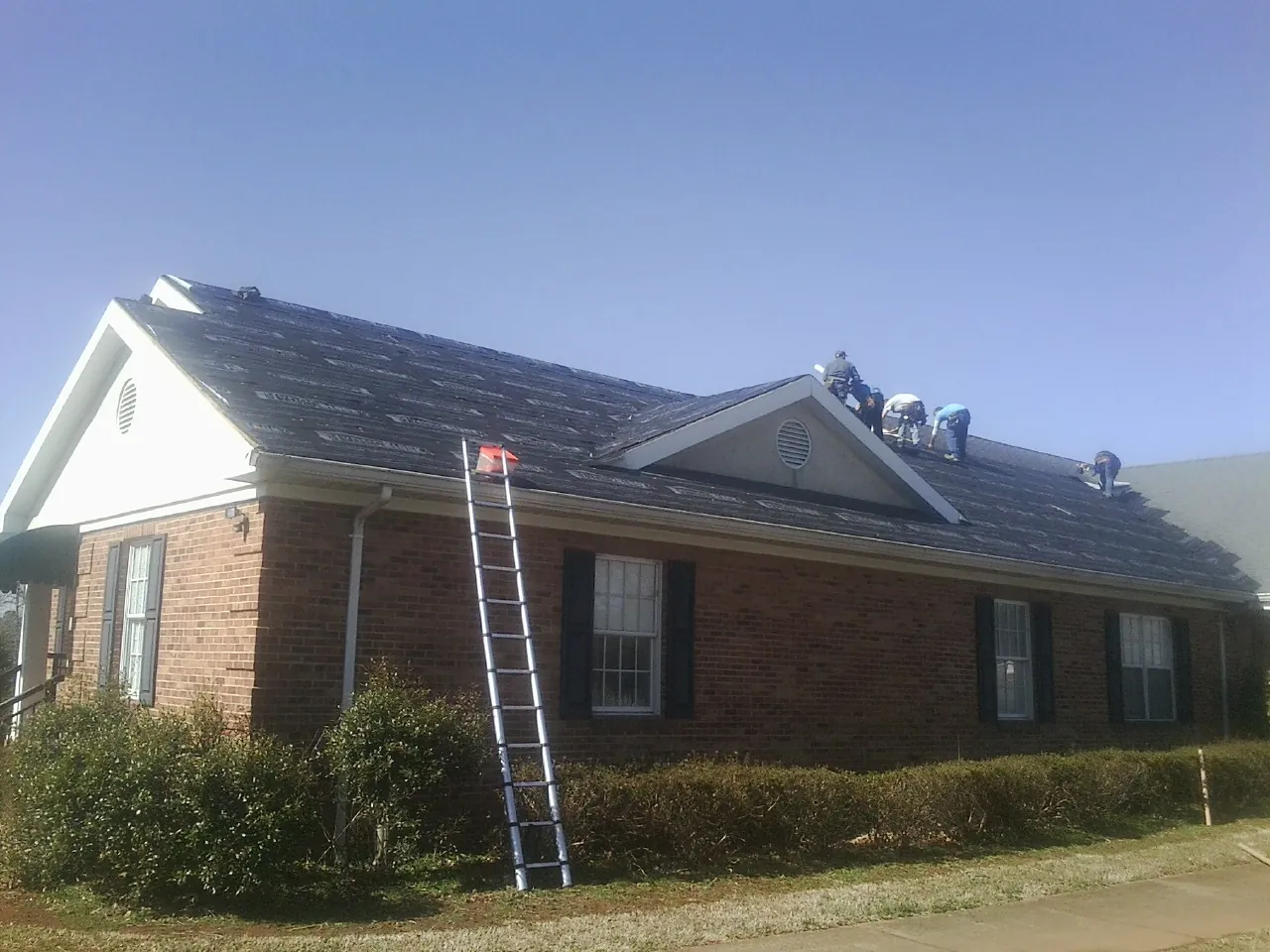Crew tearing shingles off a brick ranch roof with a ladder set — Emergency Roof Repair work by our crew in Cedarpines Park