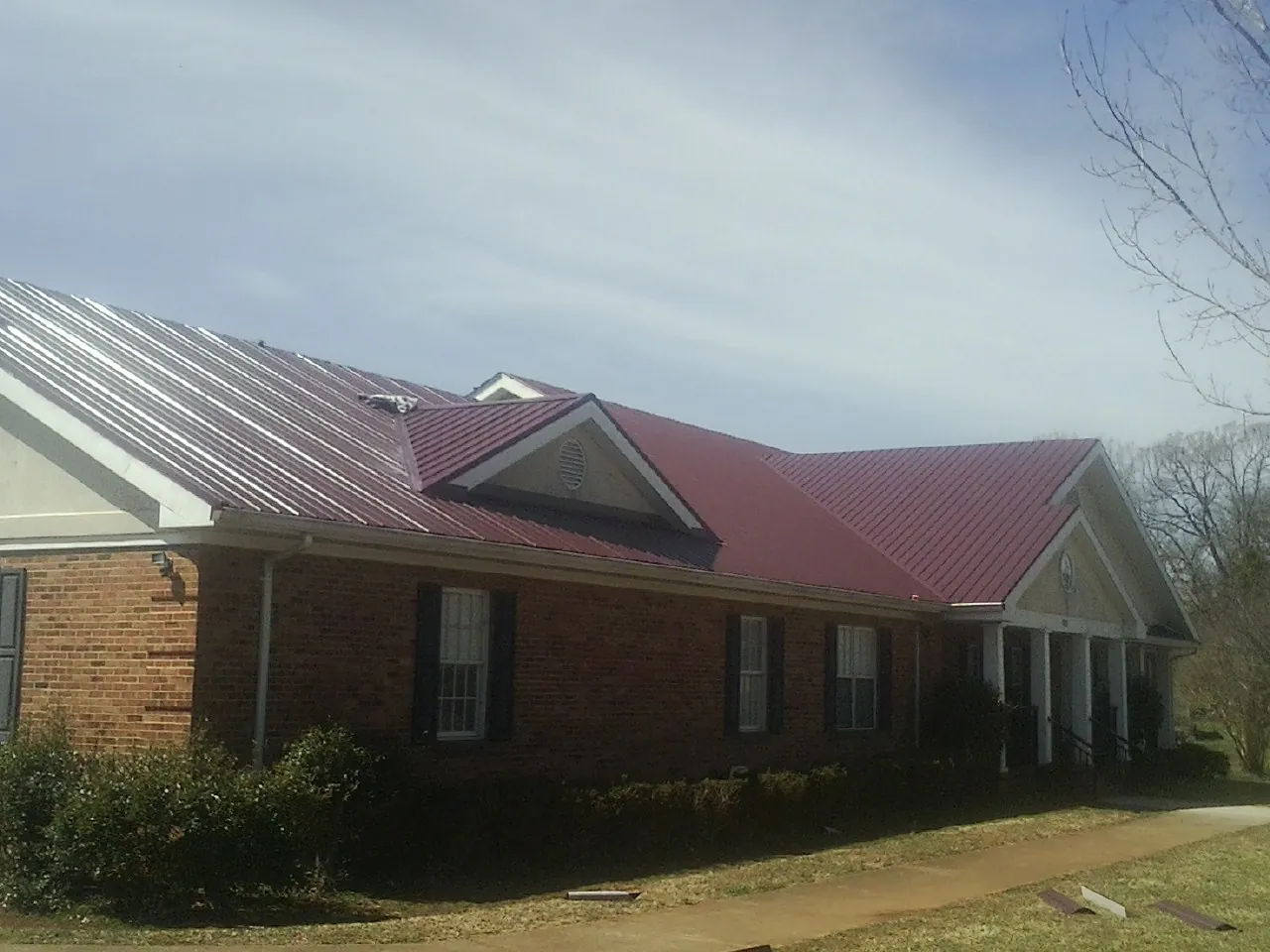 Red metal roof with gabled entries on a long brick building, from a Hail Damage Roof Repair job in Cedarpines Park