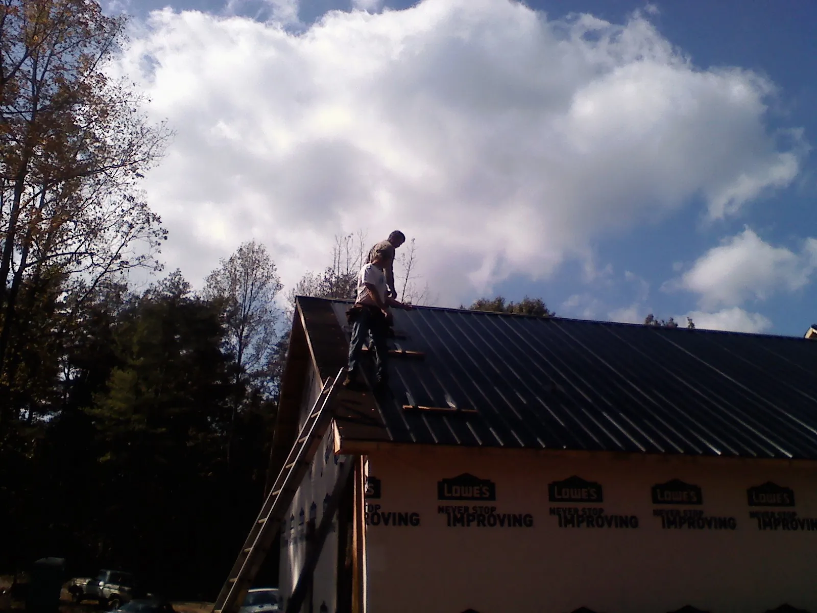Roofer fastening dark metal panels high against a cloudy sky, from a Roof Inspection job in Cedarpines Park