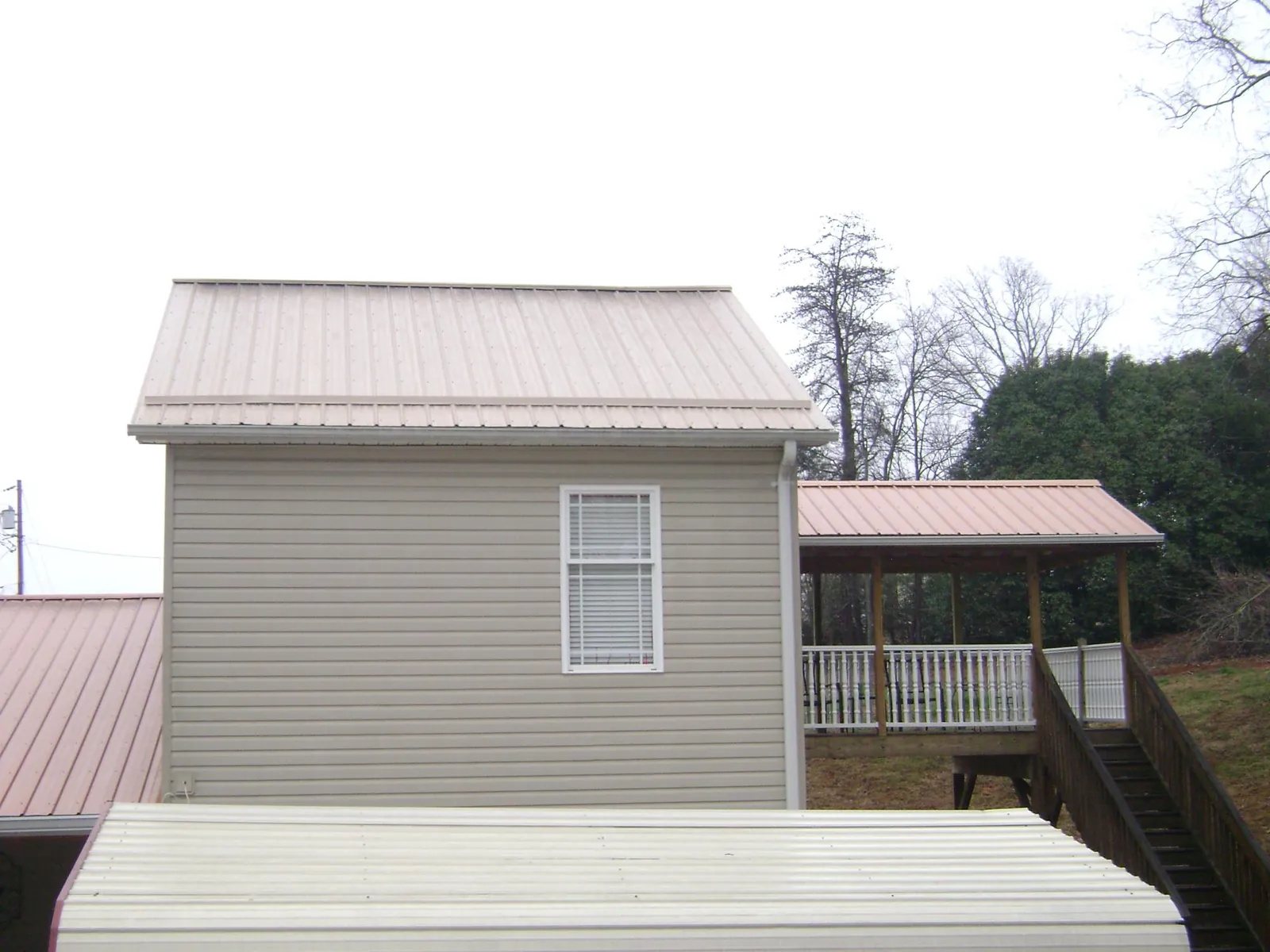 Tan metal roofs on a two story addition and attached porch, from a Roof Replacement job in Cedarpines Park
